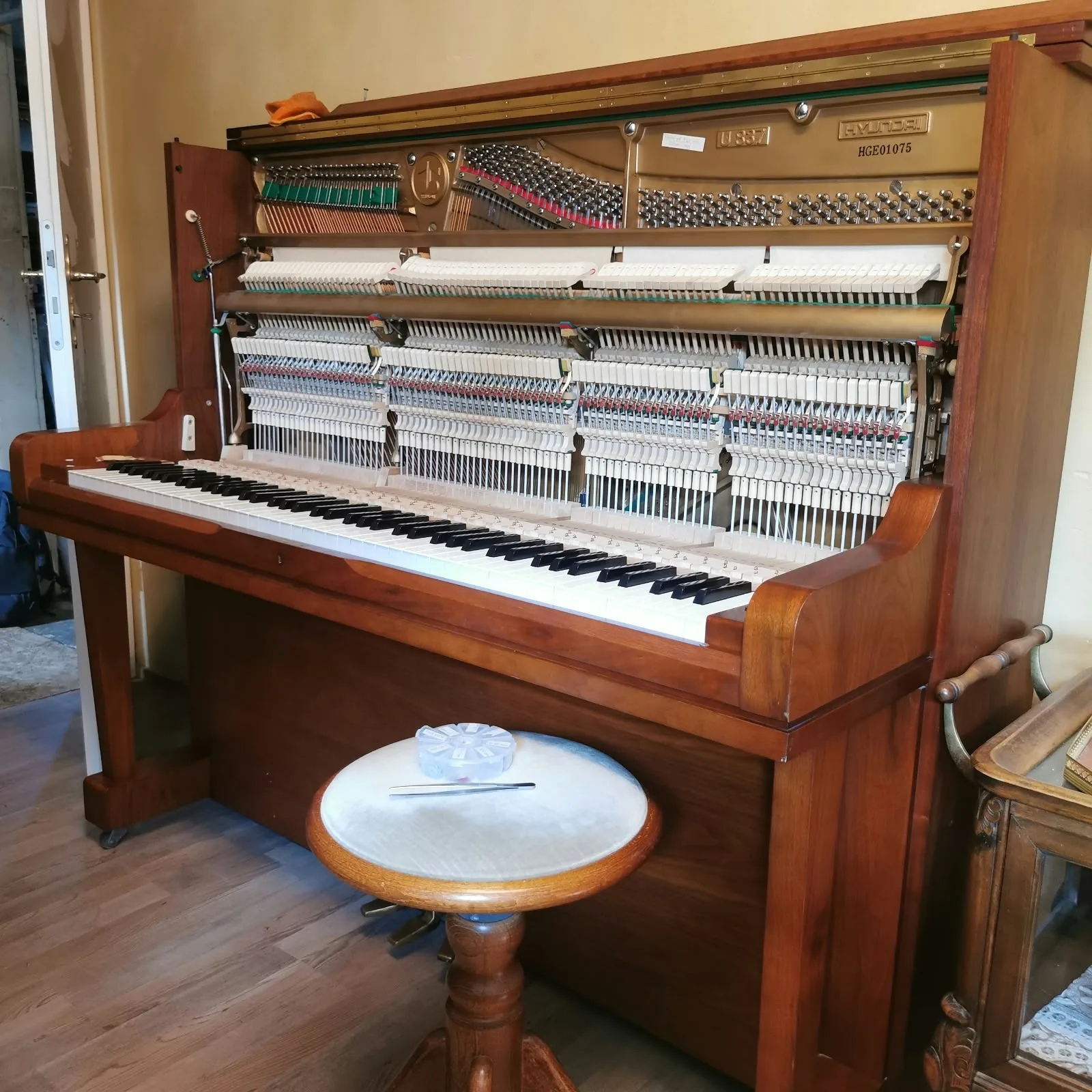 Geöffnetes Klavier mit freiliegender Mechanik und Hocker davor