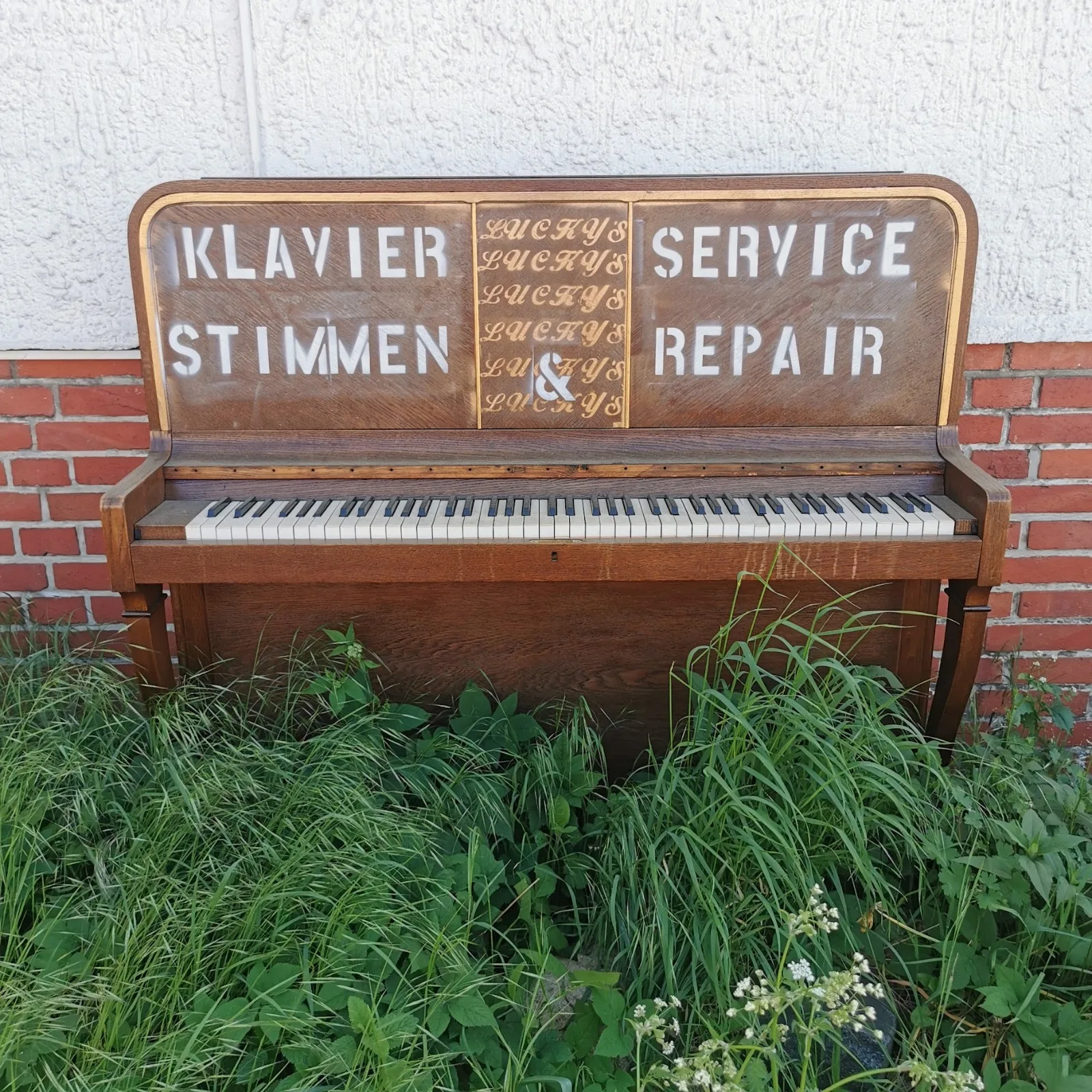 Altes Klavier im Gras mit Werbeaufschrift für den Klavierstimmdienst